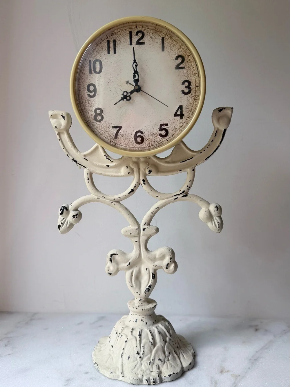 This vintage-style table clock features a distressed cream iron stand